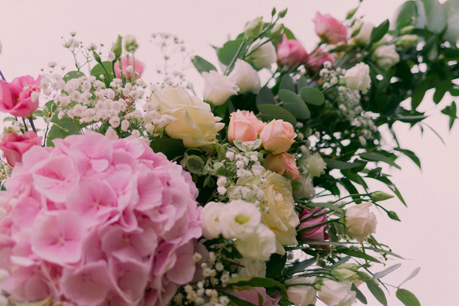 A close-up view of a floral arrangement featuring large, soft pink hydrangea blooms, creamy white roses, and delicate pale pink spray roses interspersed with sprigs of baby's breath and lush green euc